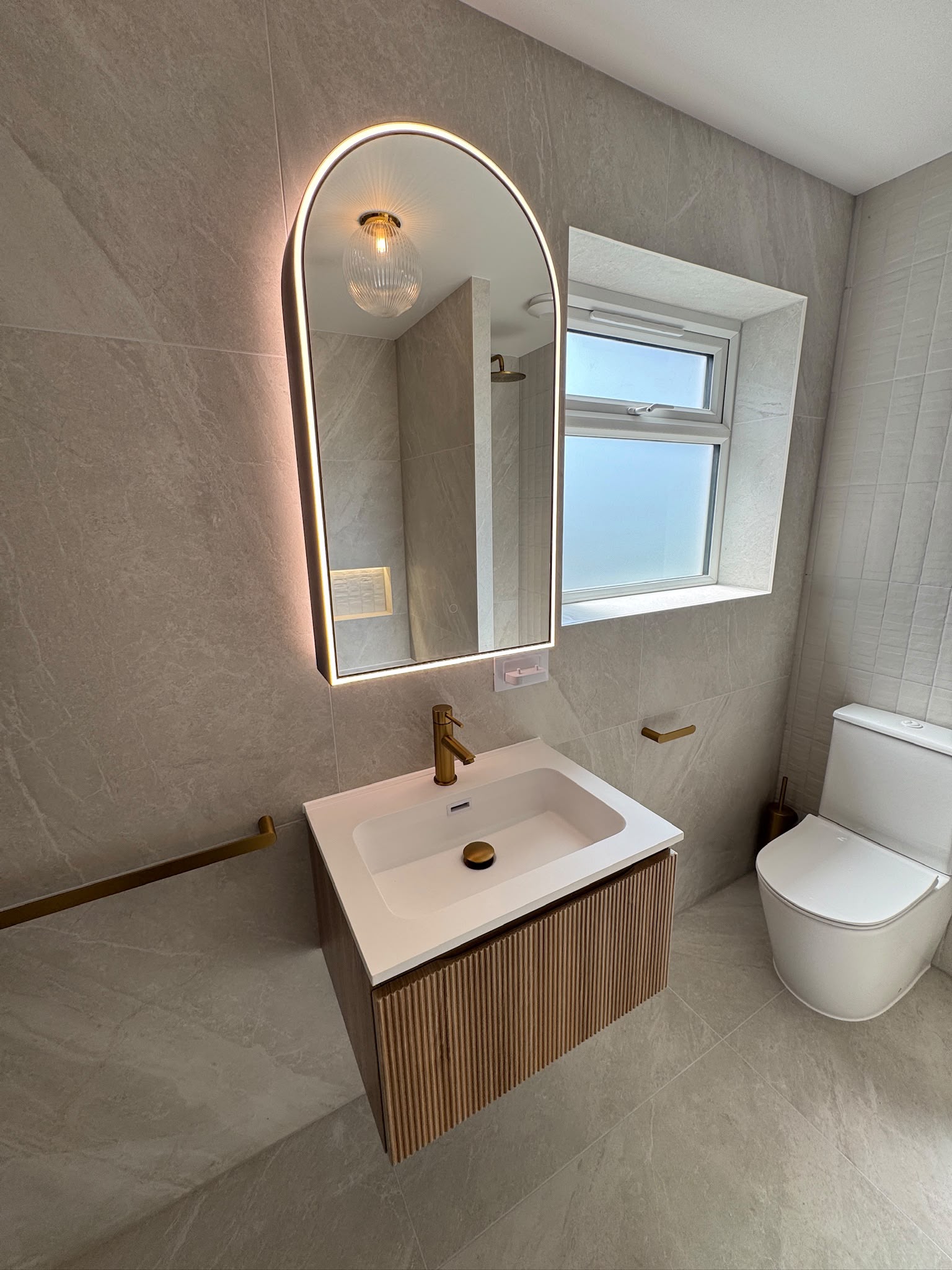 Floating vanity beneath an illuminated arched mirror