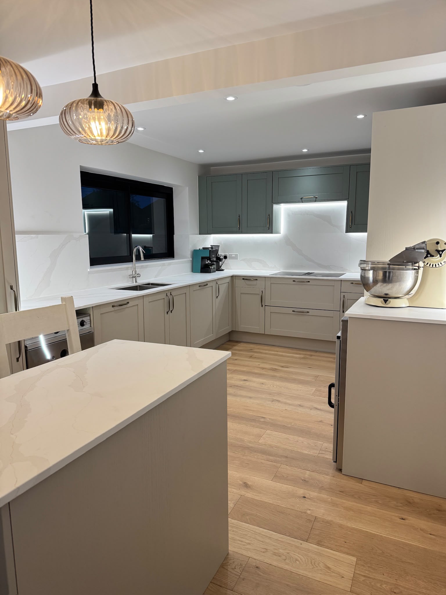Kitchen island with glass pendants and the run of shaker units beyond