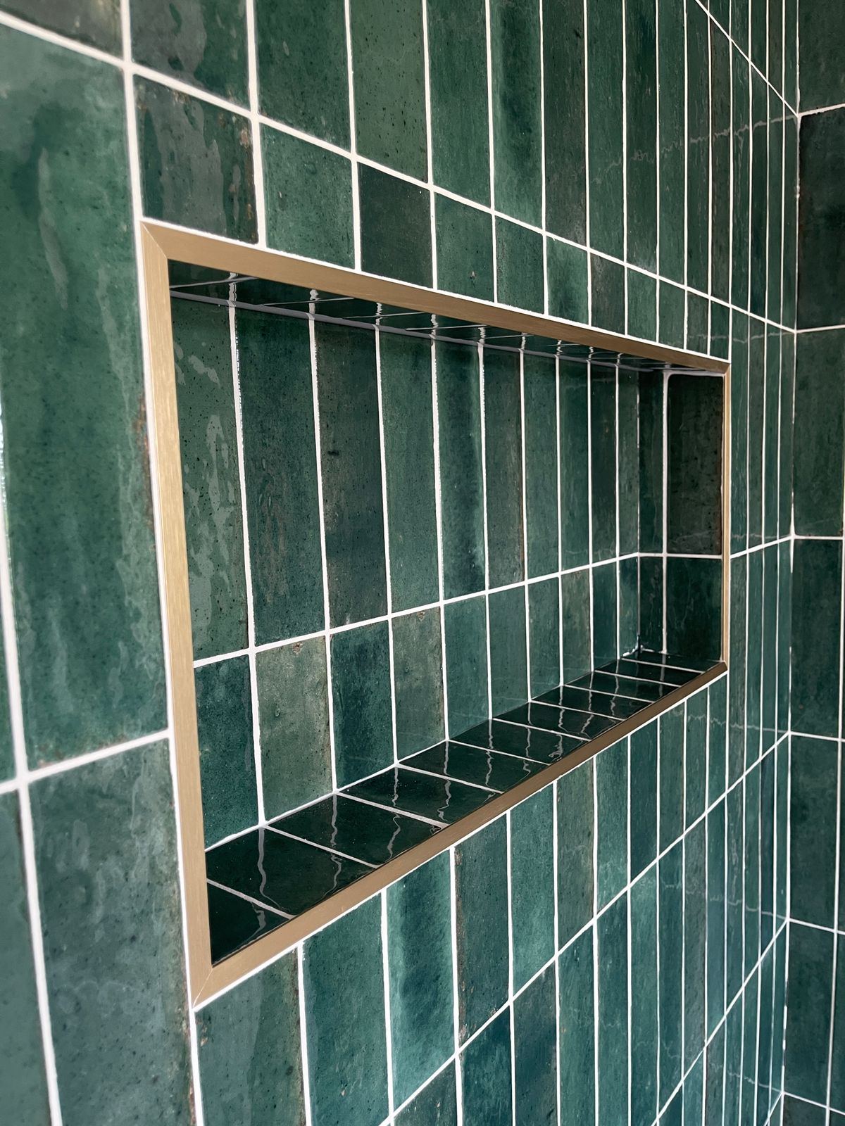 Recessed shower niche with brushed brass trim in green tiles