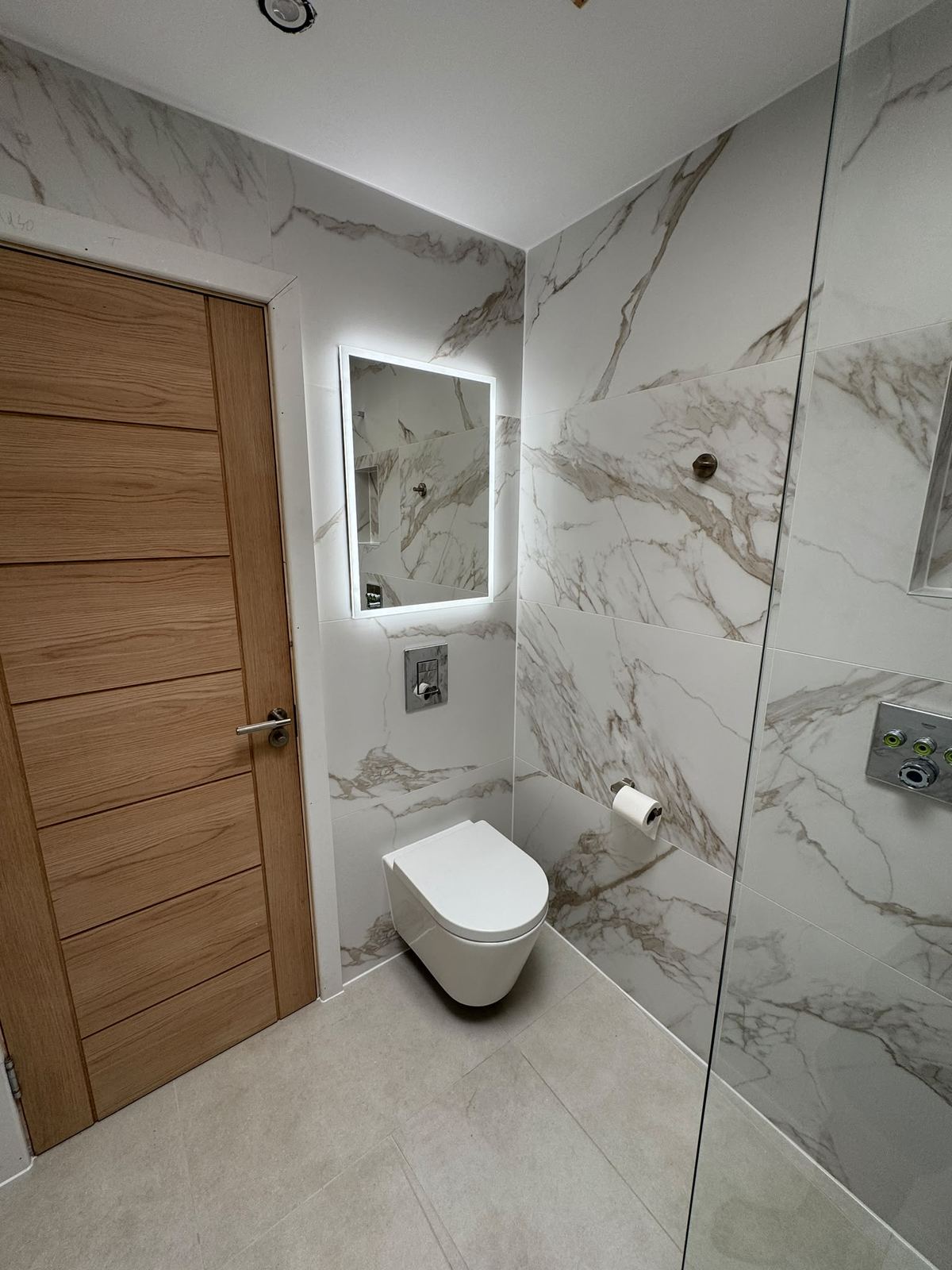 Backlit mirror and wall-hung WC beside oak door