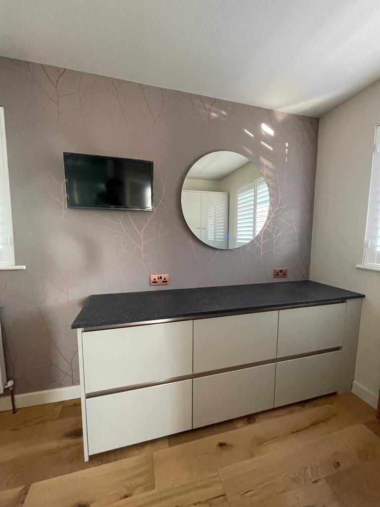 Long chest of drawers with a stone top beneath the TV and round mirror
