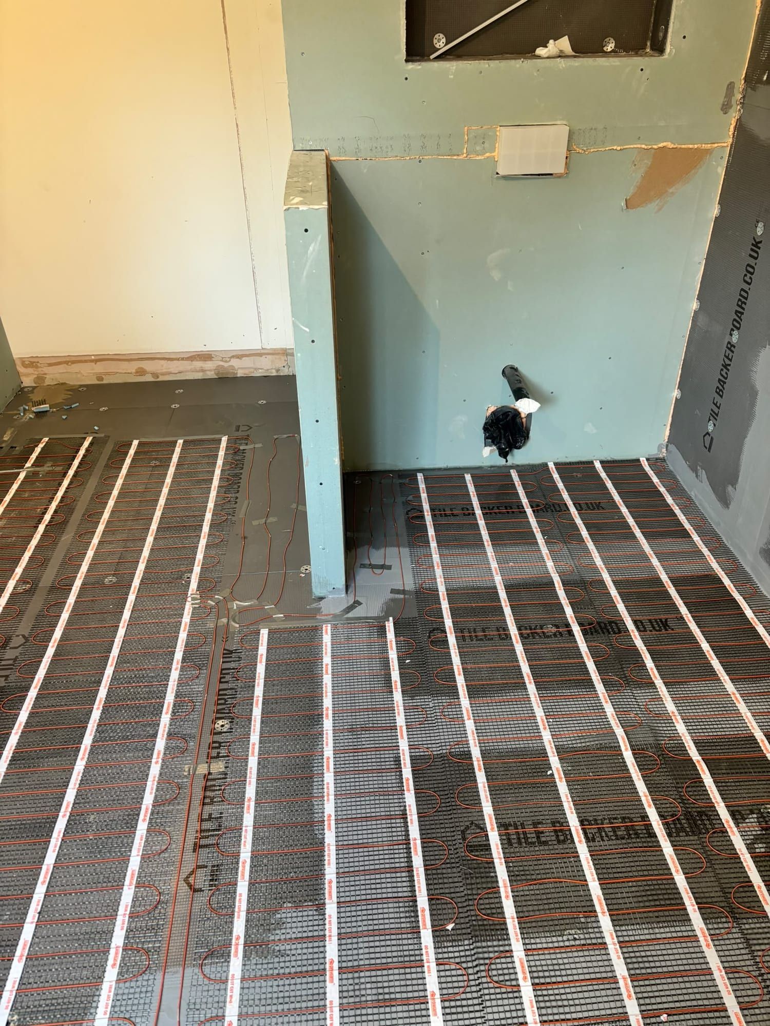 Heating mats laid across a bathroom floor in front of the boxed-in toilet frame